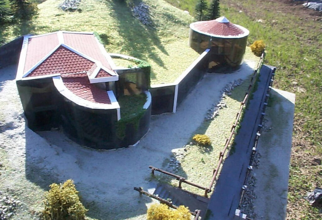 Modello in scala di una casa moderna con tetti rossi e giardino verde, visto dall'alto.