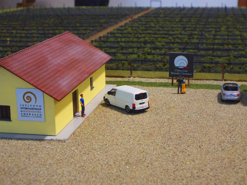 Modellino dell'Istituto di Elicicoltura a Cherasco, con auto parcheggiate e insegne visibili.