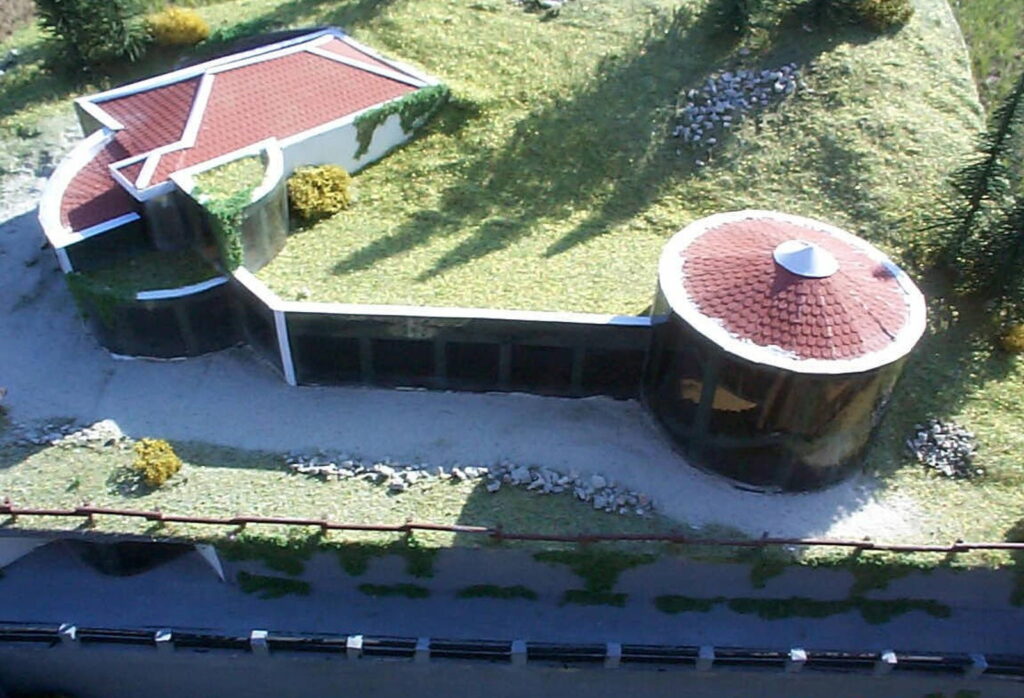 Modello in miniatura di una moderna casa circondata da vegetazione, vista dall'alto.