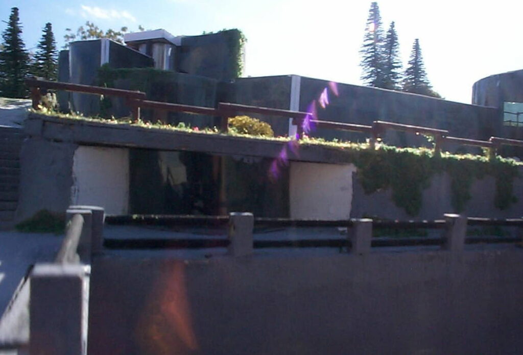 Edificio moderno con terrazza verde e piante rampicanti, alberi sullo sfondo, cielo sereno.